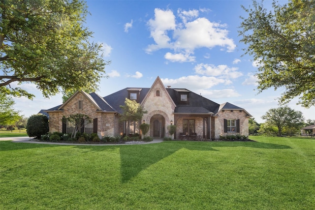 french provincial home with a front lawn and brick siding
