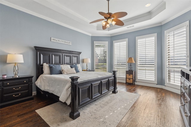 bedroom with baseboards, wood finished floors, a tray ceiling, and crown molding