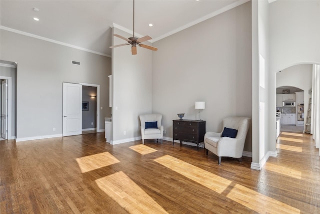 sitting room with a ceiling fan, wood finished floors, arched walkways, a high ceiling, and ornamental molding