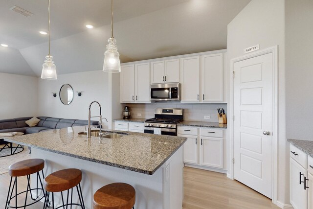 kitchen with a kitchen breakfast bar, a sink, tasteful backsplash, visible vents, and appliances with stainless steel finishes