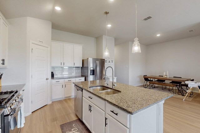 kitchen with light wood finished floors, stainless steel appliances, a sink, tasteful backsplash, and light stone counters