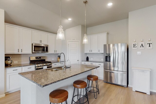 kitchen with a sink, decorative backsplash, a breakfast bar, light wood-type flooring, and stainless steel appliances