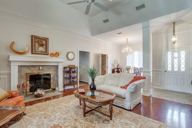 living area featuring a high end fireplace, wood finished floors, visible vents, ornamental molding, and ceiling fan with notable chandelier