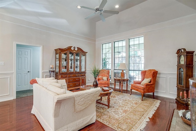 living room with a wainscoted wall, wood finished floors, a high ceiling, ceiling fan, and a decorative wall