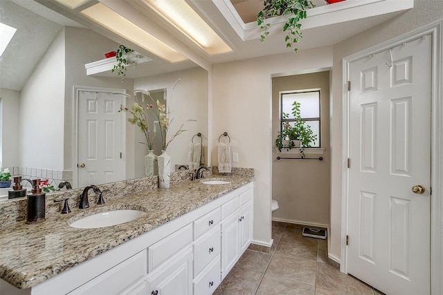 full bathroom with toilet, a sink, double vanity, and a skylight