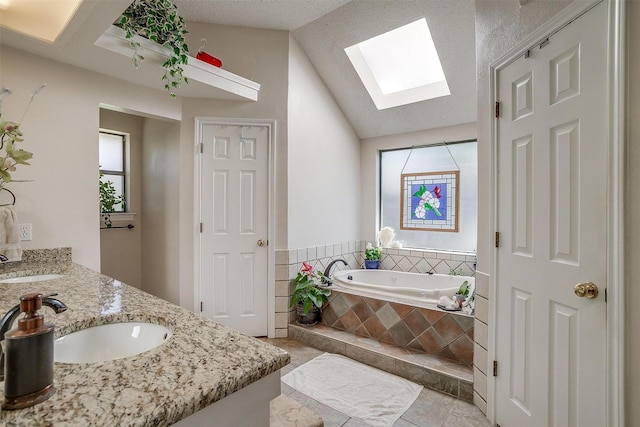 full bath with vaulted ceiling with skylight, a bath, double vanity, and a sink