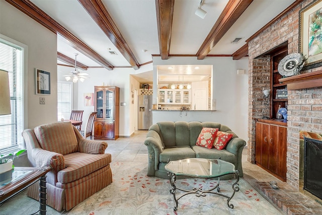 living room with beamed ceiling, ceiling fan with notable chandelier, a brick fireplace, and visible vents