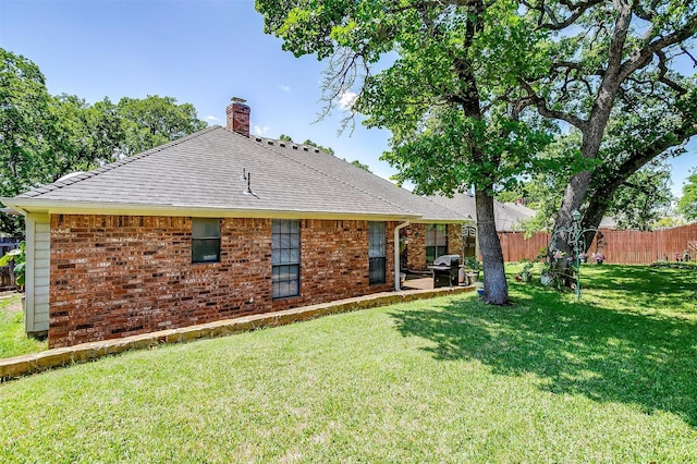 rear view of property with brick siding, a yard, a chimney, and fence