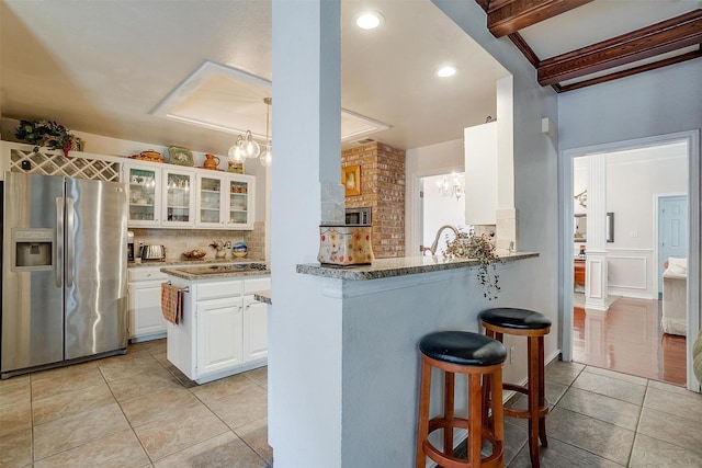 kitchen featuring decorative backsplash, glass insert cabinets, light tile patterned floors, stainless steel fridge with ice dispenser, and a kitchen bar