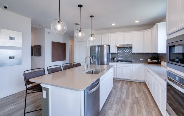 kitchen with a breakfast bar area, a sink, light wood-style floors, and appliances with stainless steel finishes