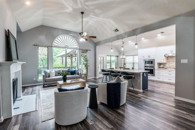 604 Lake Village Dr, Mckinney, TX 75071 - living area with ceiling fan, dark wood-style flooring, a fireplace with raised hearth, baseboards, and high vaulted ceiling