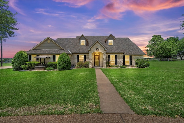 french country style house featuring a lawn, stone siding, and a shingled roof