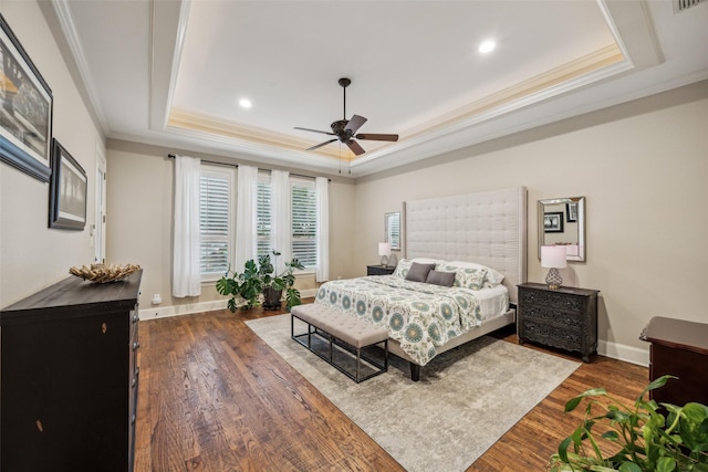 bedroom with dark wood-type flooring, a raised ceiling, ornamental molding, and recessed lighting