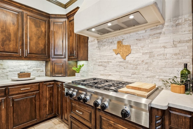 kitchen featuring decorative backsplash, light countertops, stainless steel gas cooktop, and wall chimney exhaust hood