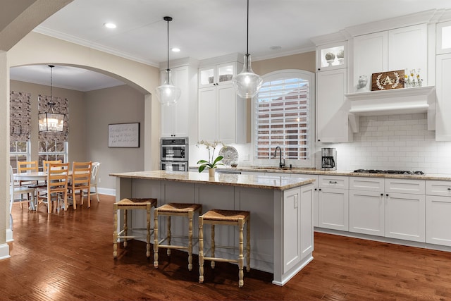 kitchen with white cabinets, arched walkways, backsplash, a kitchen island, and appliances with stainless steel finishes