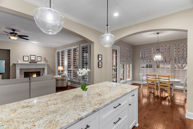 kitchen featuring white cabinets, arched walkways, light stone counters, decorative light fixtures, and dark wood-type flooring