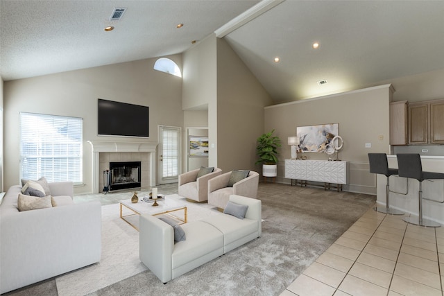living area with high vaulted ceiling, light tile patterned flooring, light carpet, a tile fireplace, and visible vents