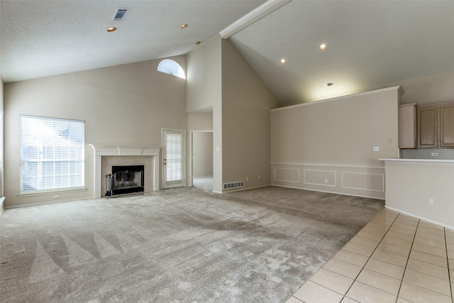 unfurnished living room featuring light carpet, a tile fireplace, visible vents, and high vaulted ceiling