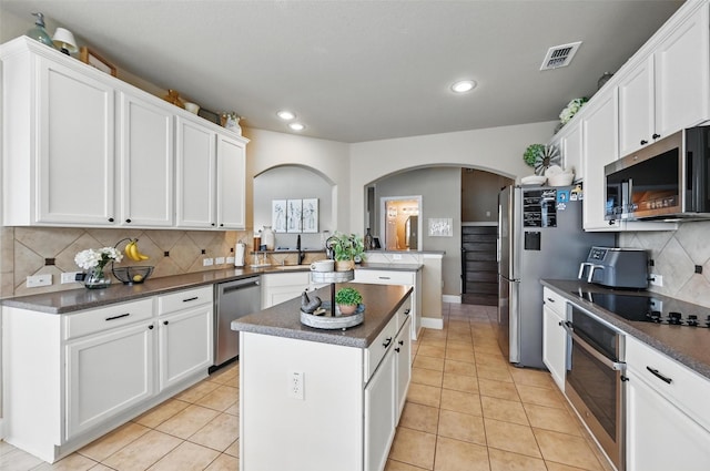 kitchen with dark countertops, arched walkways, stainless steel appliances, a kitchen island, and recessed lighting