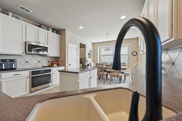 kitchen featuring decorative backsplash, dark countertops, stainless steel appliances, and visible vents