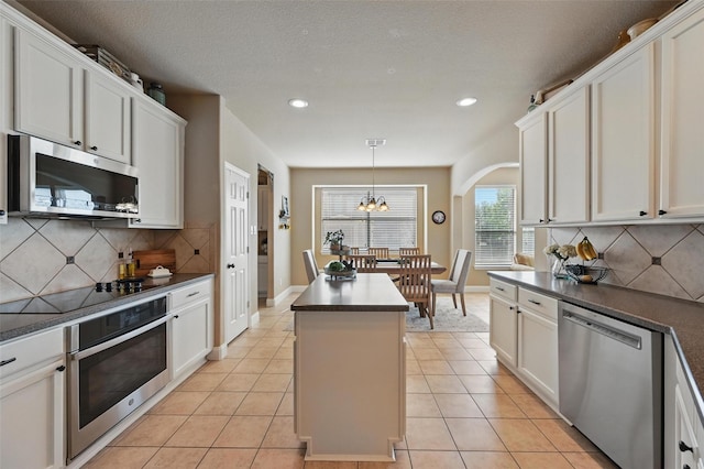 kitchen with arched walkways, dark countertops, a center island, and stainless steel appliances