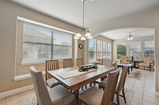 dining space featuring arched walkways, light tile patterned flooring, ceiling fan with notable chandelier, and baseboards
