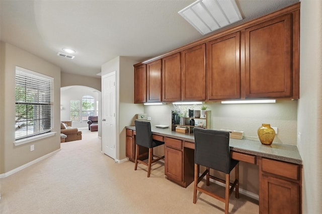 office featuring built in study area, visible vents, light carpet, baseboards, and arched walkways