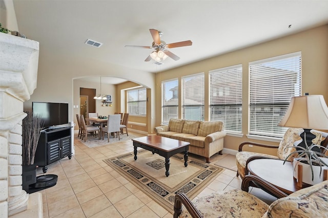 living area featuring a ceiling fan, light tile patterned floors, arched walkways, baseboards, and visible vents