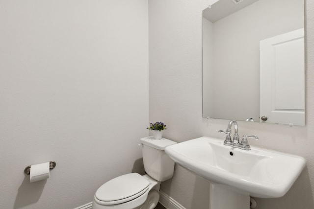 half bath featuring baseboards, a sink, and toilet