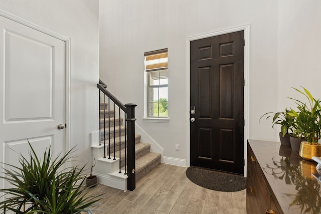 foyer entrance featuring light wood finished floors, baseboards, and stairs