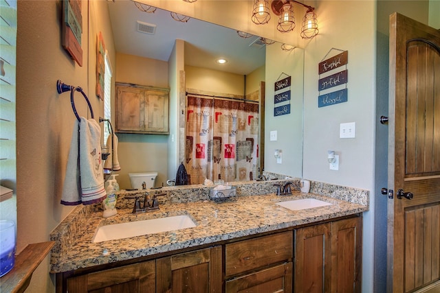 bathroom with double vanity, visible vents, toilet, and a sink