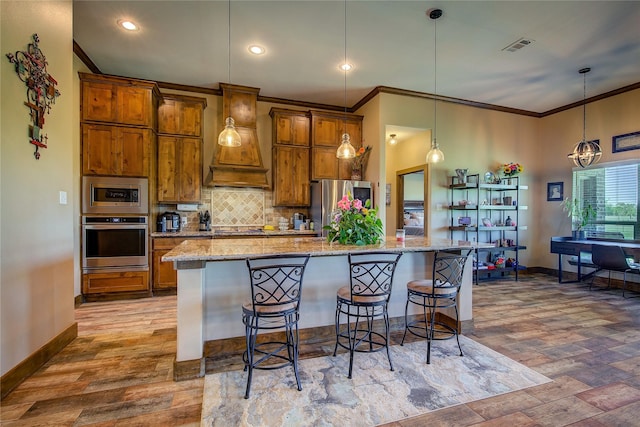 kitchen with a kitchen breakfast bar, brown cabinets, crown molding, appliances with stainless steel finishes, and premium range hood