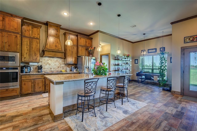 kitchen featuring a kitchen breakfast bar, brown cabinets, ornamental molding, premium range hood, and appliances with stainless steel finishes