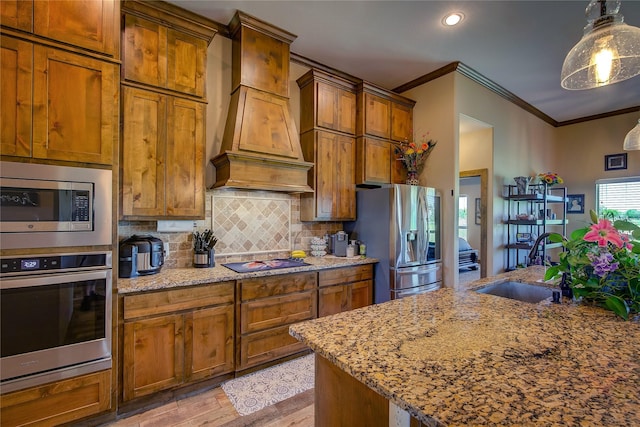 kitchen featuring custom exhaust hood, crown molding, a sink, brown cabinets, and appliances with stainless steel finishes