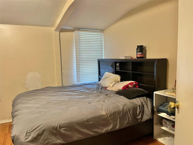 bedroom with vaulted ceiling, wood finished floors, and baseboards