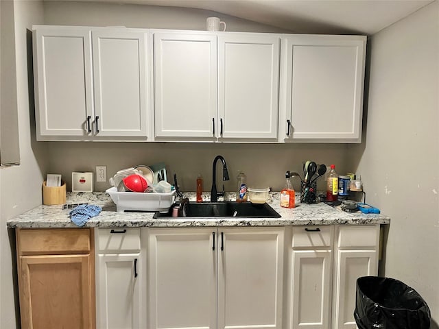 kitchen featuring a sink, white cabinetry, and light stone counters