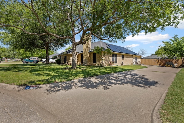 view of front of property with brick siding, solar panels, fence, and a front lawn
