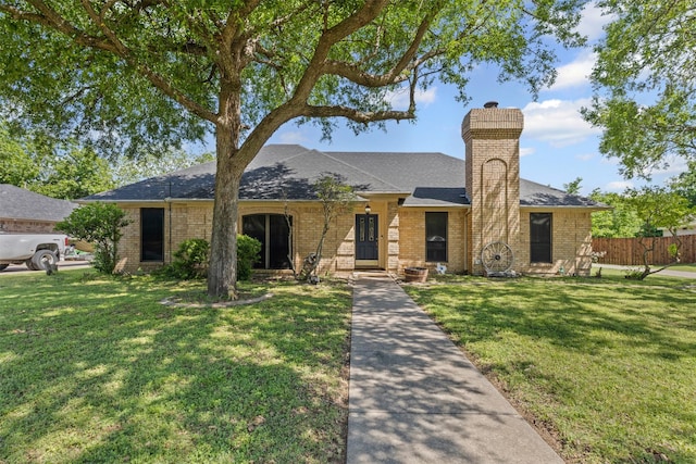 ranch-style home featuring fence, a chimney, brick siding, and a front yard