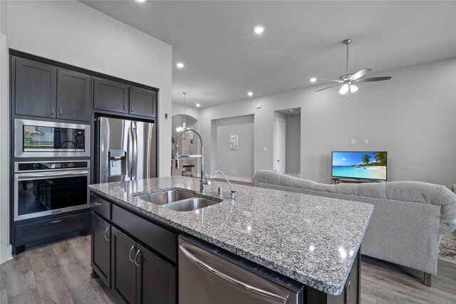 kitchen featuring stainless steel appliances, a sink, light wood-type flooring, a kitchen island with sink, and open floor plan