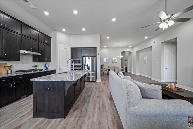 kitchen featuring light wood finished floors, a sink, arched walkways, appliances with stainless steel finishes, and open floor plan