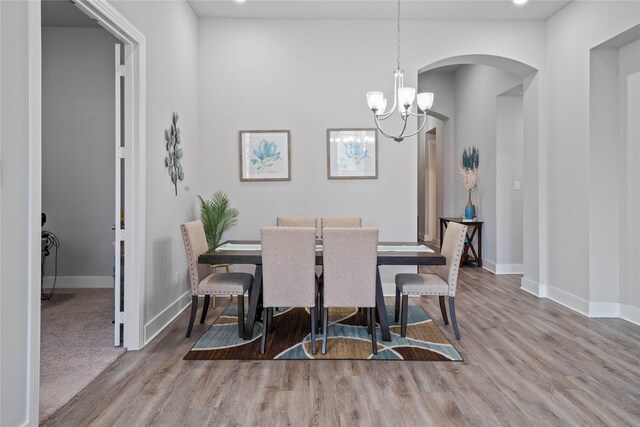 dining room featuring arched walkways, wood finished floors, baseboards, and a notable chandelier