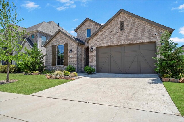 french provincial home with concrete driveway, brick siding, a front yard, and a garage