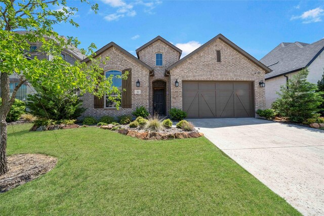 french country inspired facade with an attached garage, driveway, a front lawn, and brick siding
