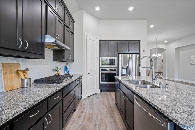 kitchen featuring light stone counters, a sink, a chandelier, appliances with stainless steel finishes, and under cabinet range hood
