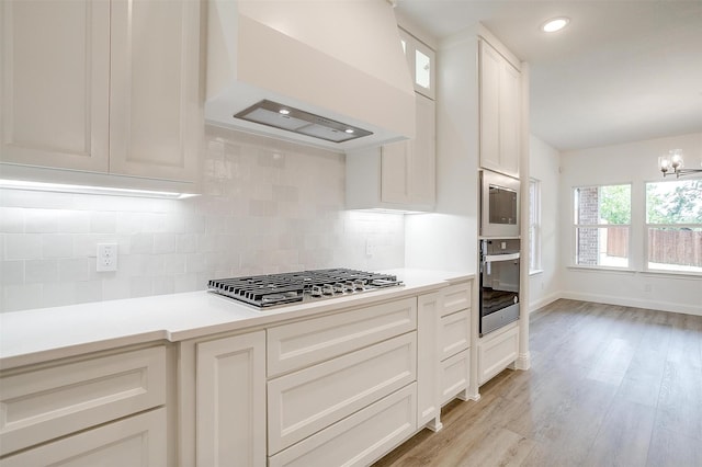 kitchen featuring light wood-type flooring, stainless steel appliances, decorative backsplash, and premium range hood