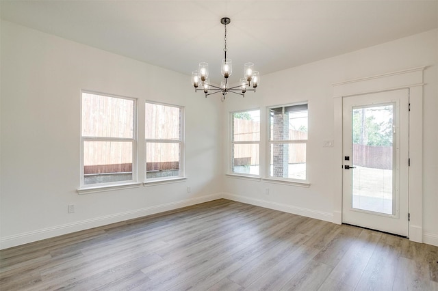 unfurnished dining area with a wealth of natural light, wood finished floors, a chandelier, and baseboards