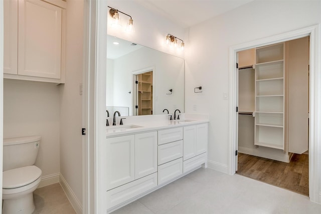 full bathroom with a walk in closet, toilet, a sink, and double vanity