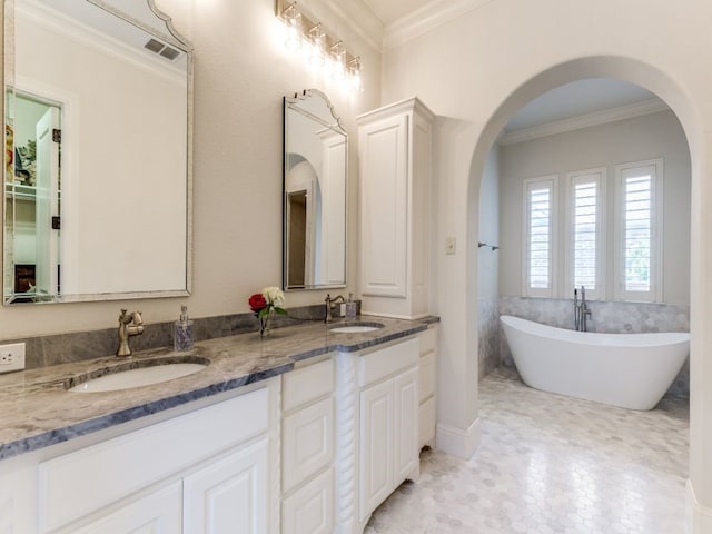 bathroom with a freestanding tub, visible vents, crown molding, and a sink