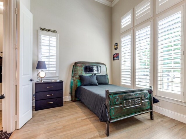 bedroom featuring crown molding, multiple windows, light wood-style flooring, and baseboards