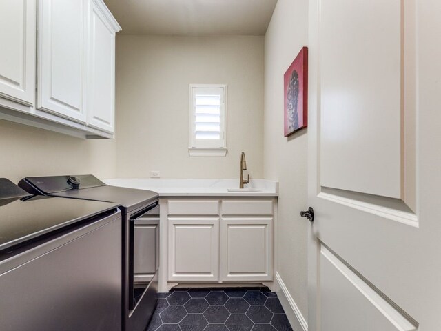 laundry area with dark tile patterned floors, washer and dryer, cabinet space, and a sink